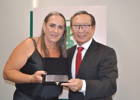 Lucinéia Romanini Sakashita, esposa do Dr. Alichandre Fumio Sakashita, recebe a placa de homenagem do Dr. Thomas Kim